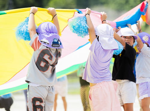子どもたちが屋外でカラフルな布を持ち上げて遊んでいる様子