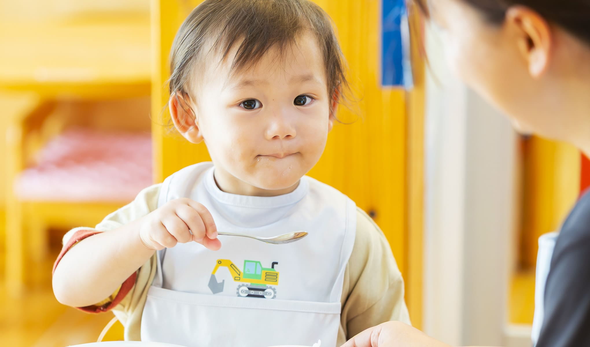 幼児がスプーンを手に持ち、ごはんを食べている場面