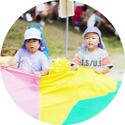 カラフルなパラバルーンを使って屋外で遊ぶ子どもたちの姿