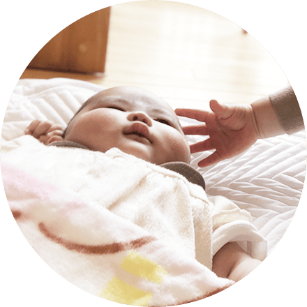 布団に寝かされた赤ちゃんにそっと触れる手が映るやさしい場面