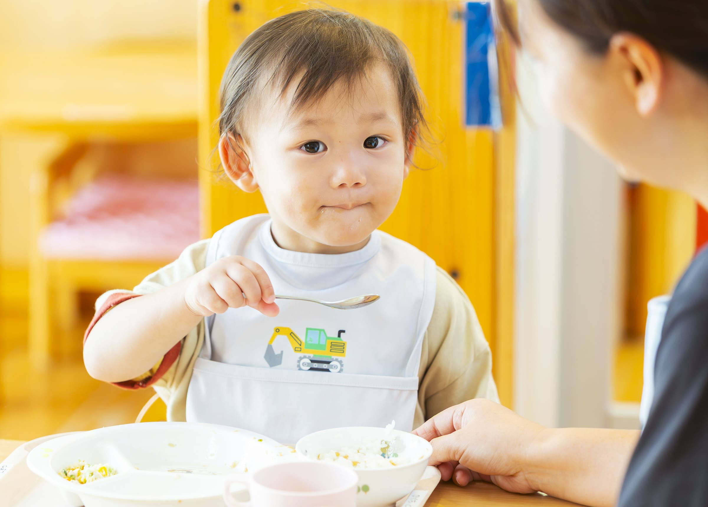 幼児がスプーンを手に持ち、ごはんを食べている場面