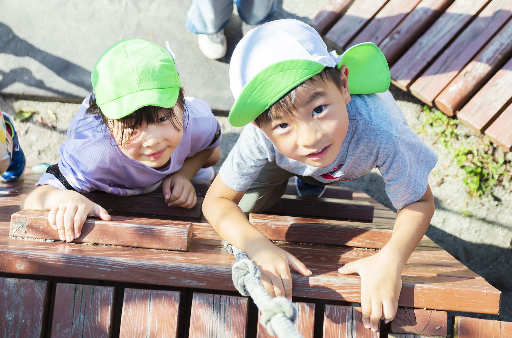 ロープを使って木製の遊具を登っている2人の子どもたち