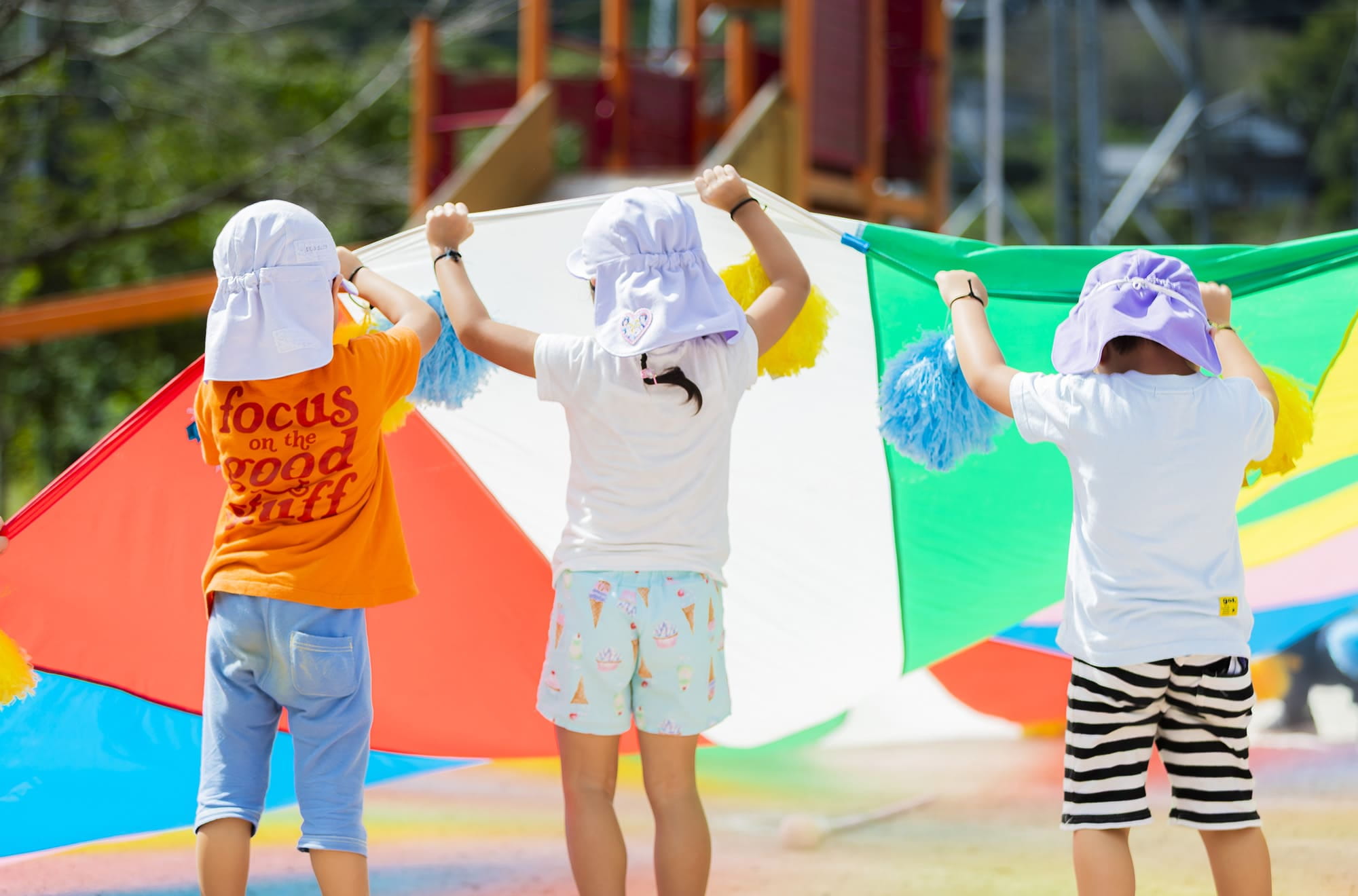 大きなカラフルな布を3人の子どもが持ち上げている様子