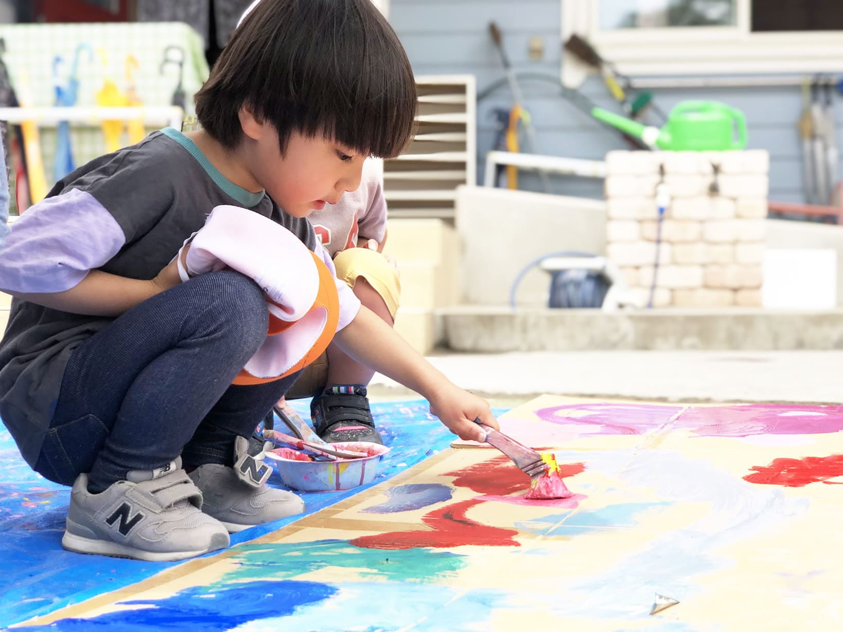 屋外で大きな紙に絵の具を使って絵を描く子どもの真剣な様子